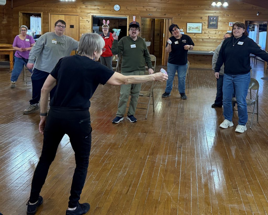 Woman in all black attire directs a group of men and women in a Mindful Movement activity.